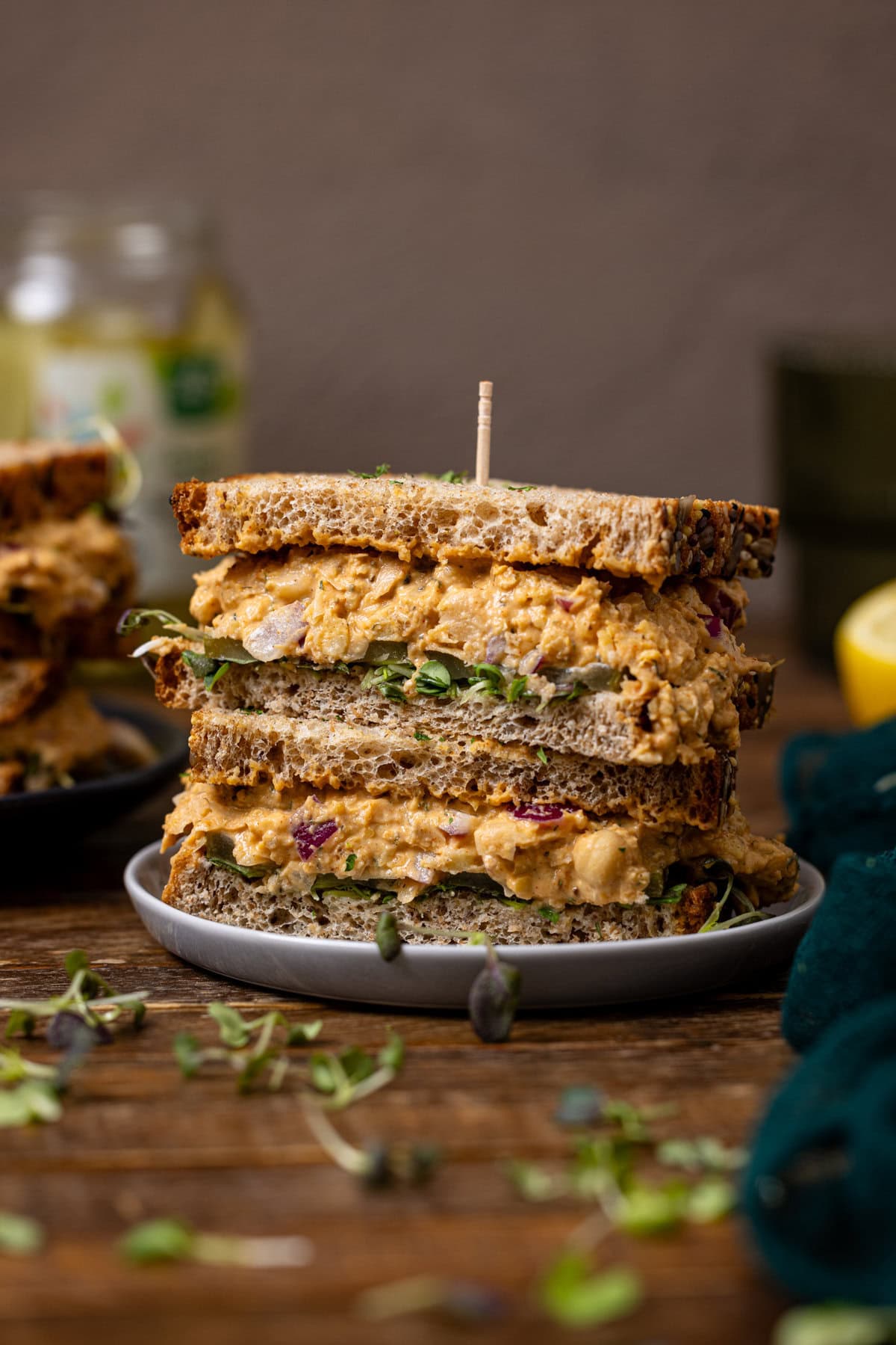 Chickpea tuna salad sandwiches stacked with more sandwiches + pickles in the background.