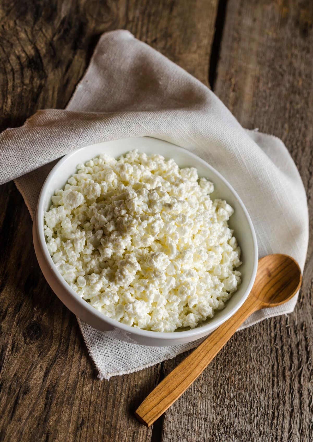 Cottage cheese in a white bowl with a brown wooden spoon.