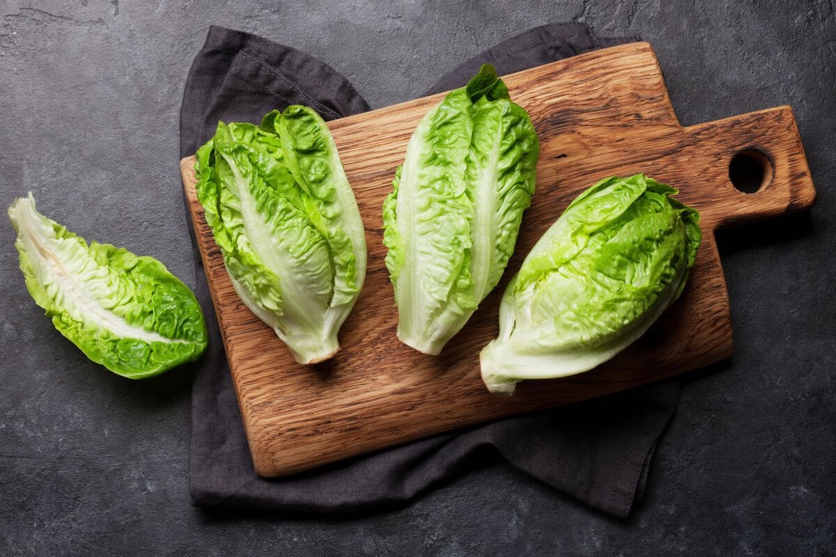 Green whole romaine lettuce on wooden chopping board.