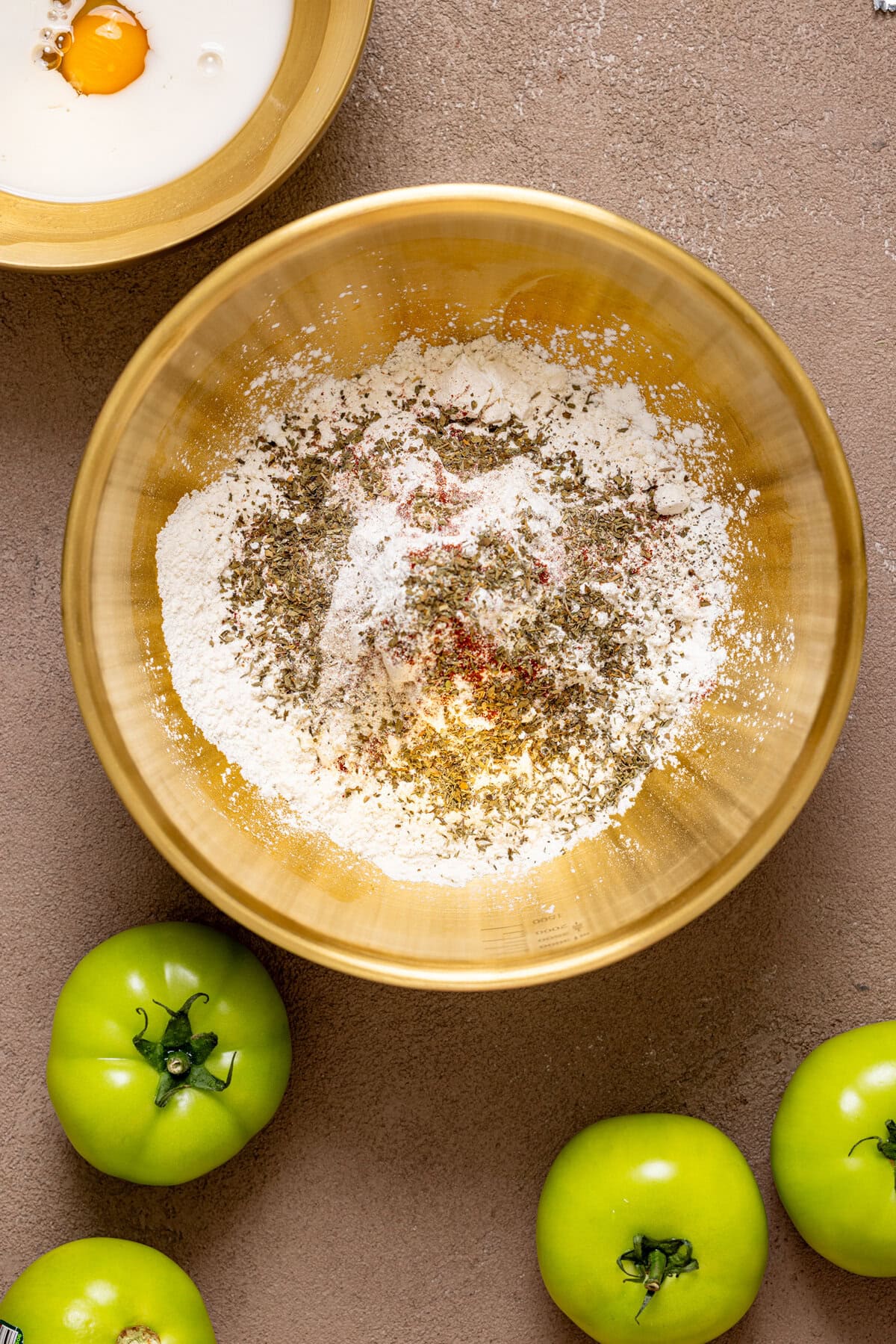 Seasoned flour in a gold bowl with green tomatoes.