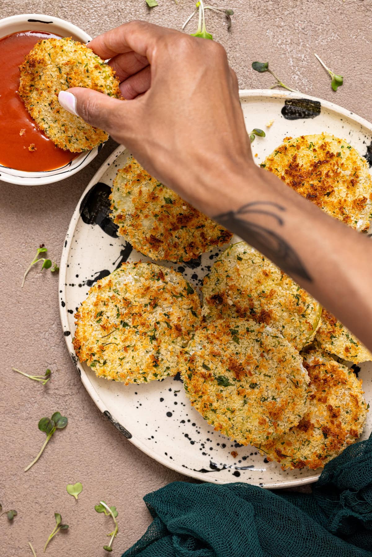 A plate with fried tomatoes and one being dipped in red sauce with hands.