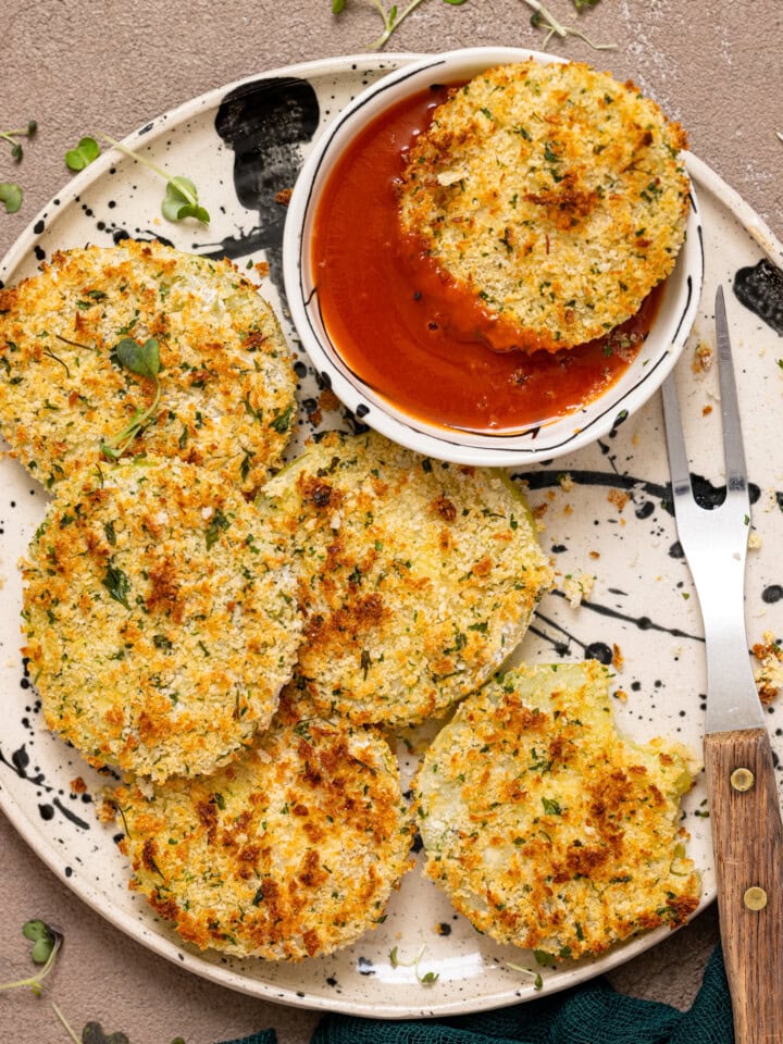 Fried green tomato on a plate, dipped in red sauce, and with a fork.