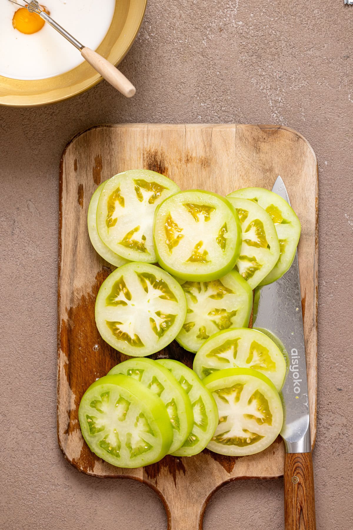 Sliced green tomatoes on a cutting board with a knife.