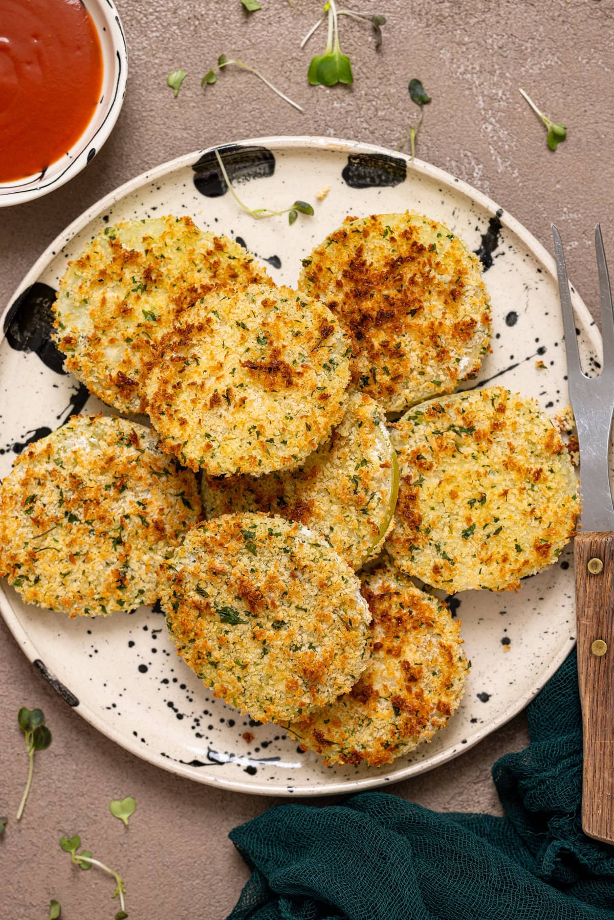 Fried green tomatoes on a black + white plate with a fork and bowl of red dipping sauce.