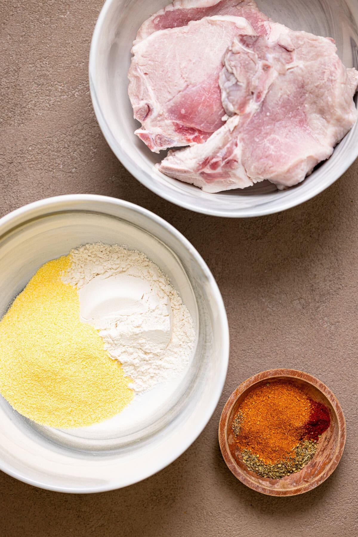 A bowl with clean pork chops and seasoning and flour.