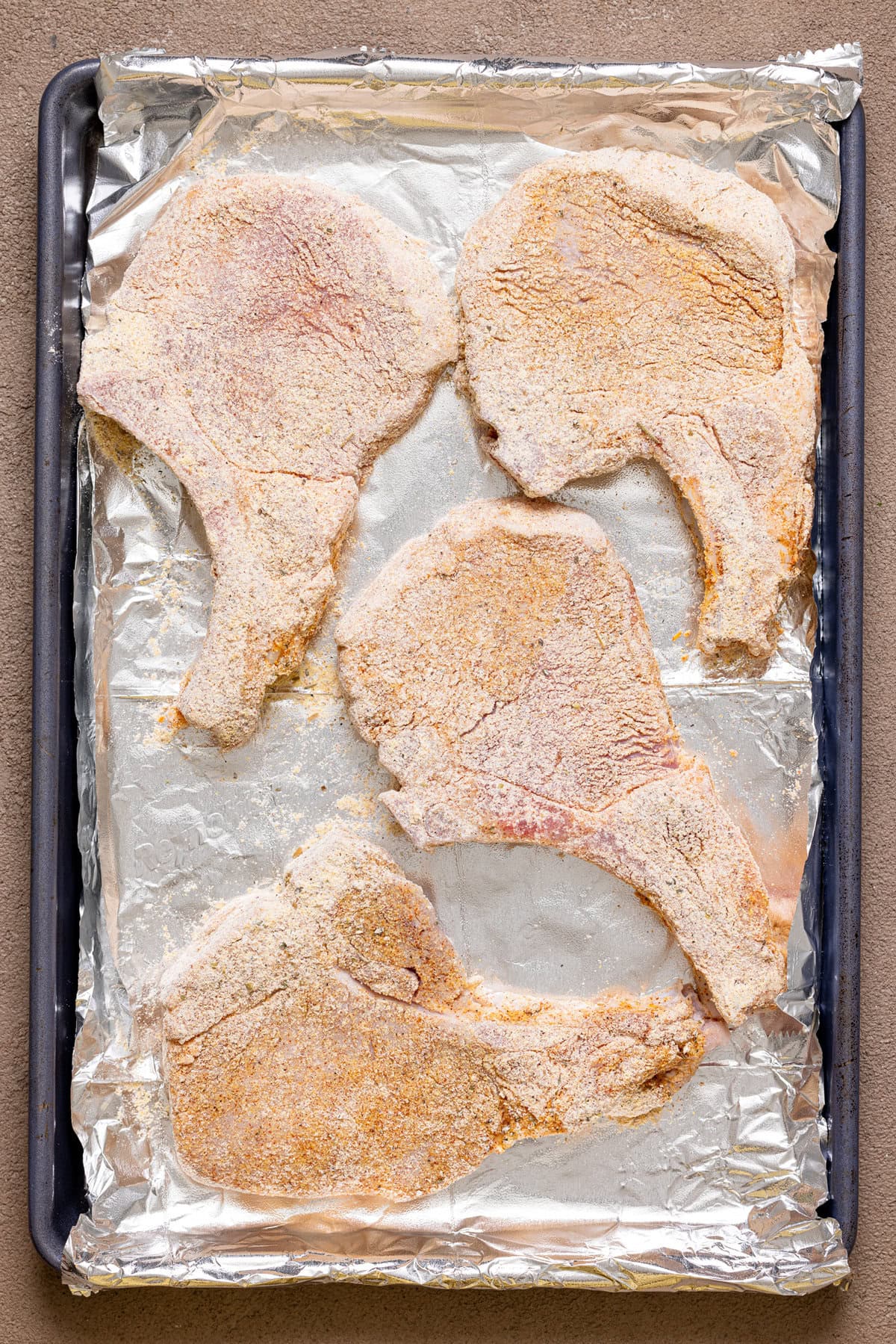 Coated pork chops lined on a baking sheet with foil paper.