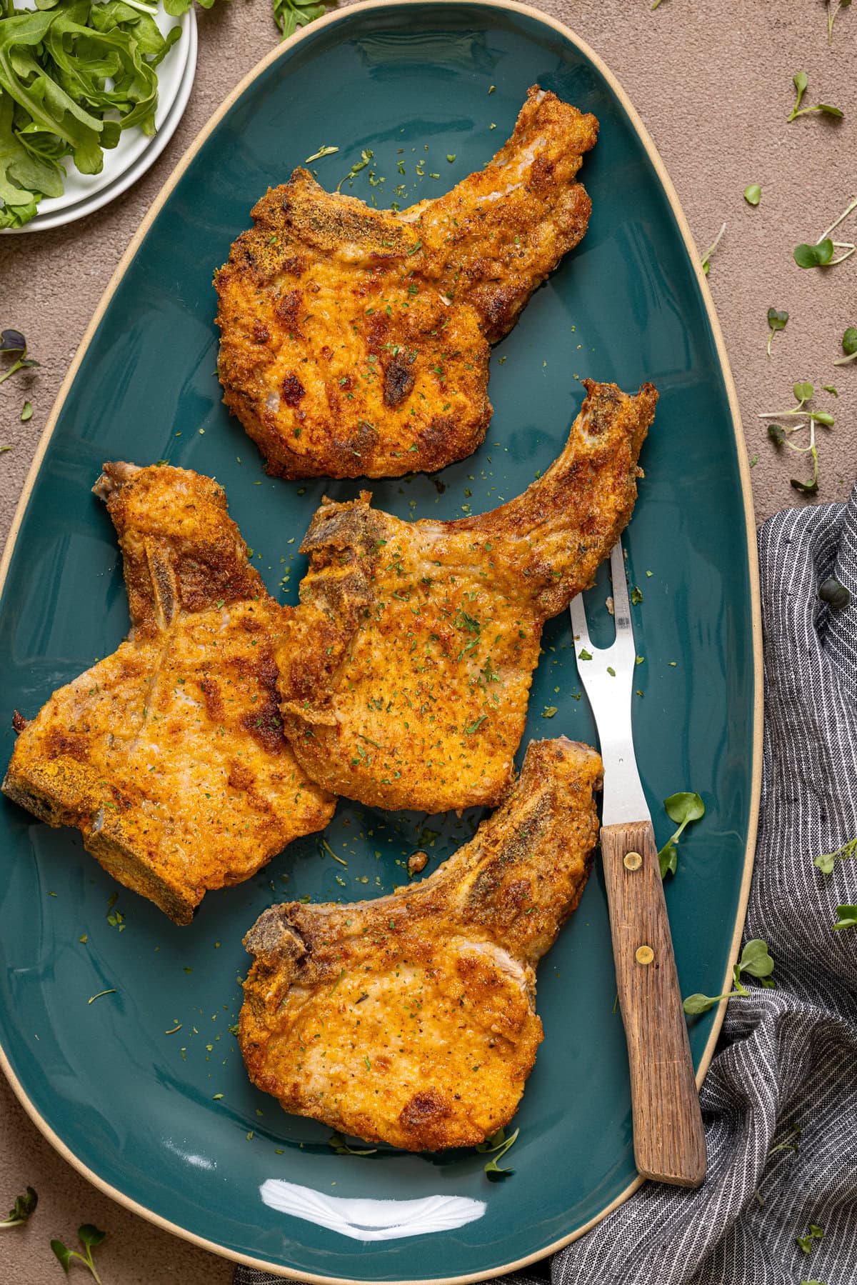 Fried pork chops on a blue platter with fork.