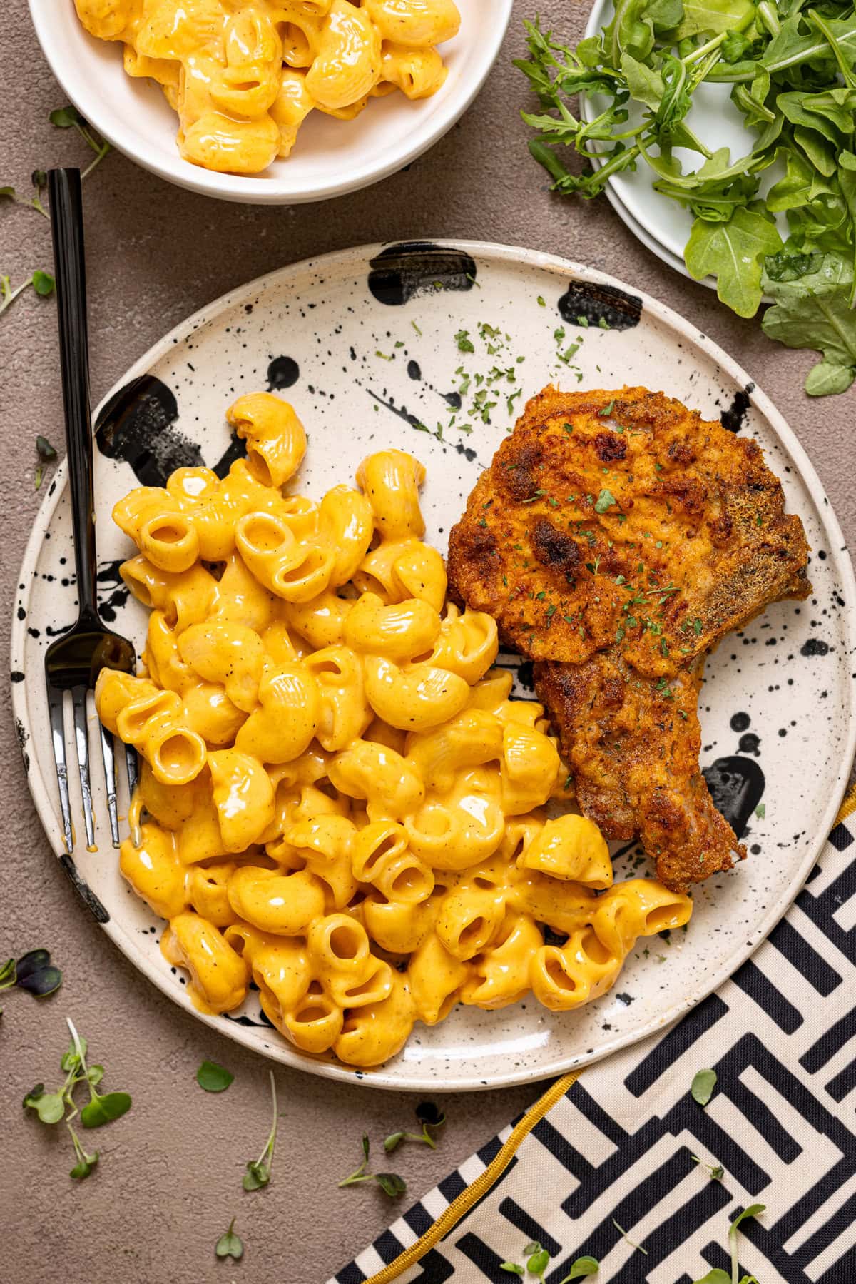 Plate with porks chops and mac and cheese with a fork and side of greens.