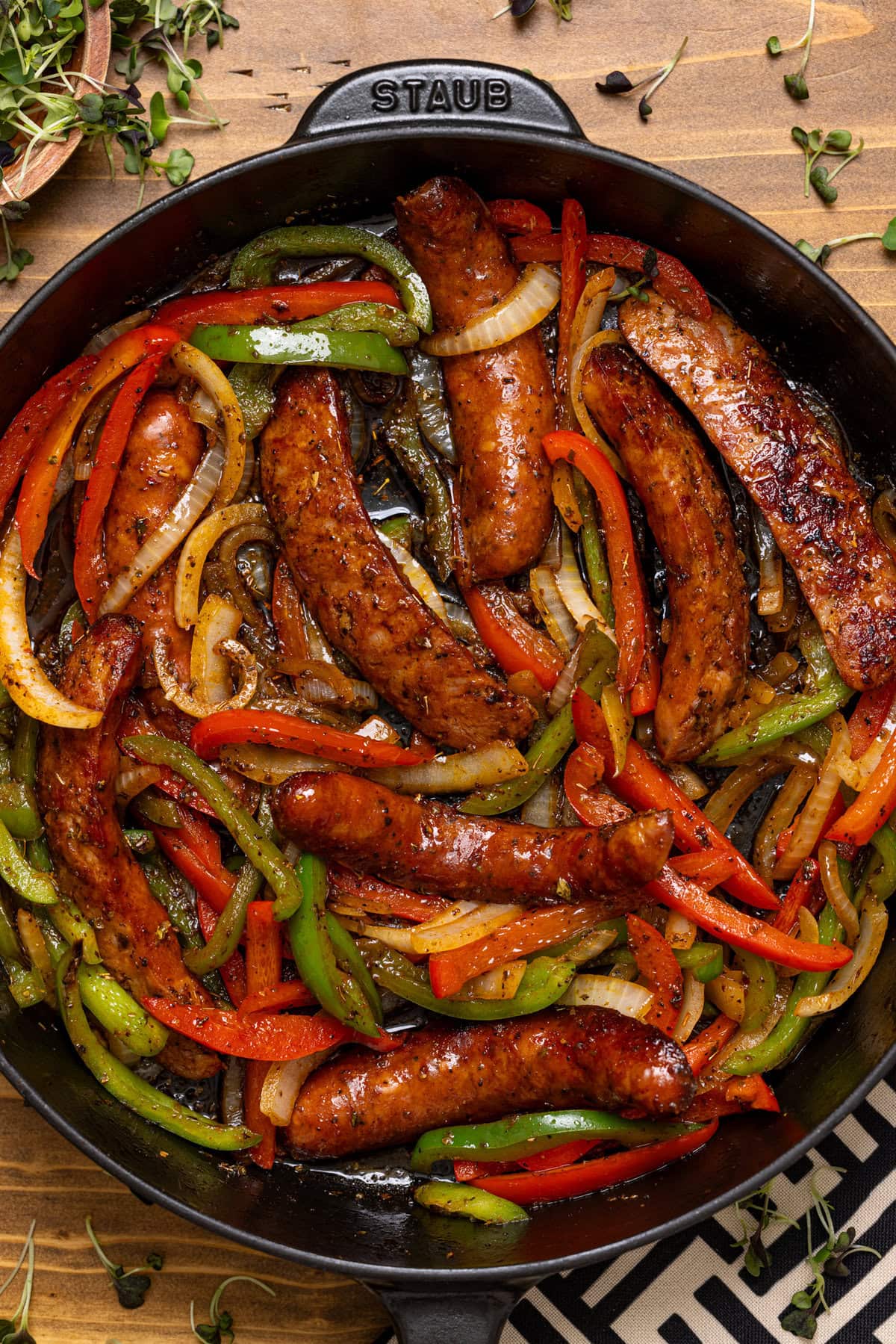 Sausage and peppers in a black skillet on a brown wood table for weeknight dinner.