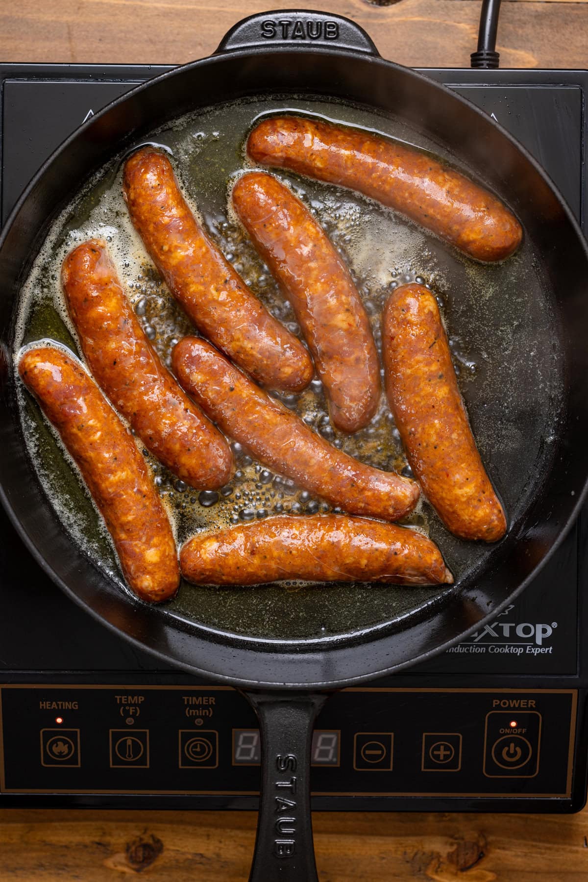 Sausages being seared in a black skillet over the stovetop.