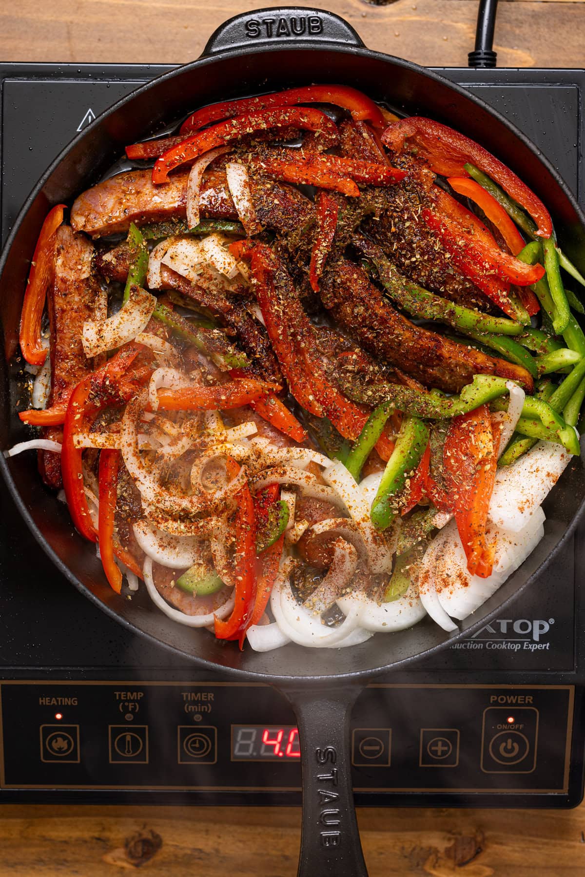 Sausages, peppers, and onions in a skillet being seared over the stovetop.