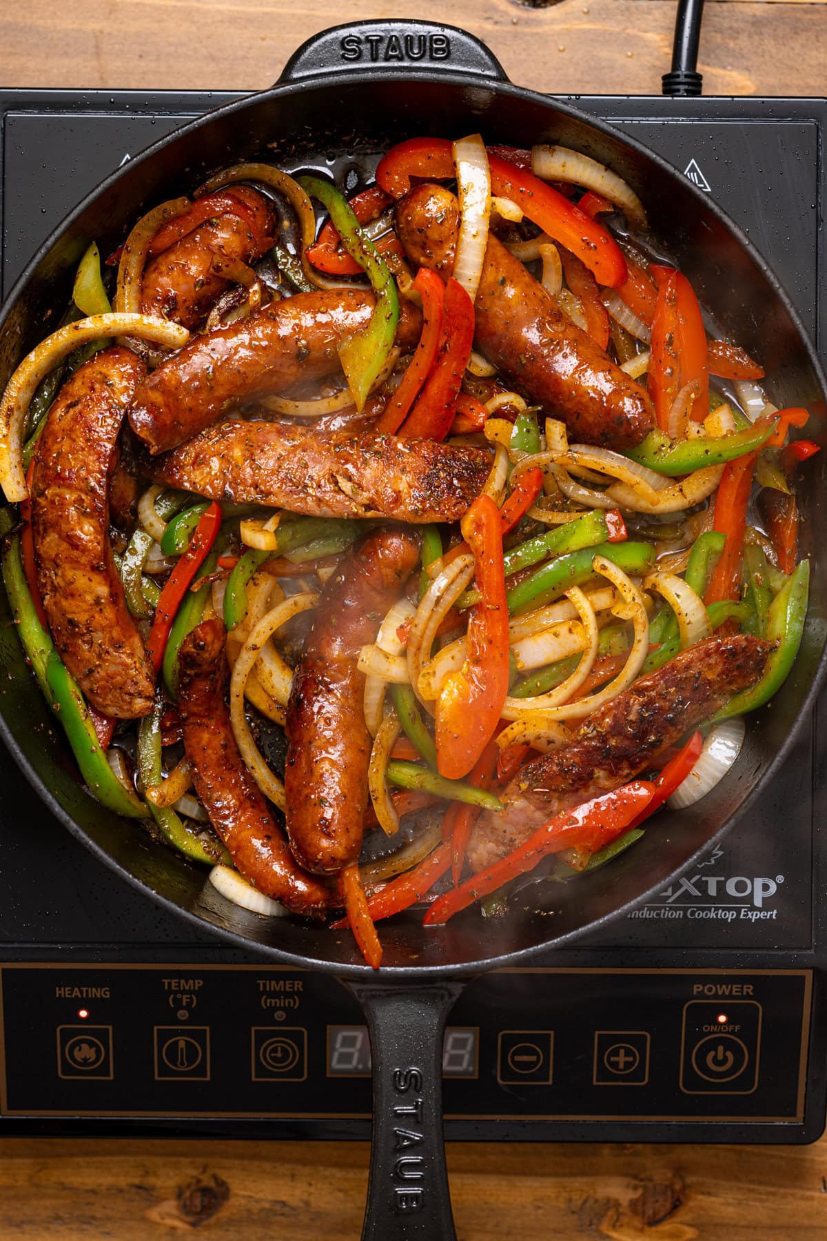 Seared sausages, peppers, and onions in a skillet. 