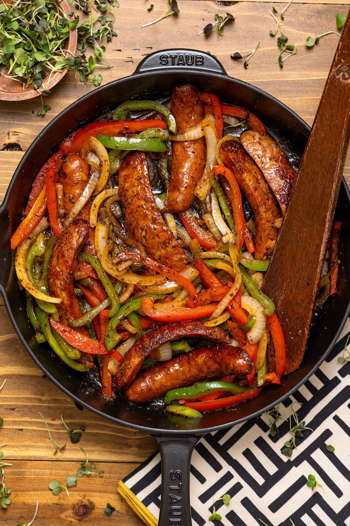 Sausage and peppers in a black skillet with a wooden spoon.