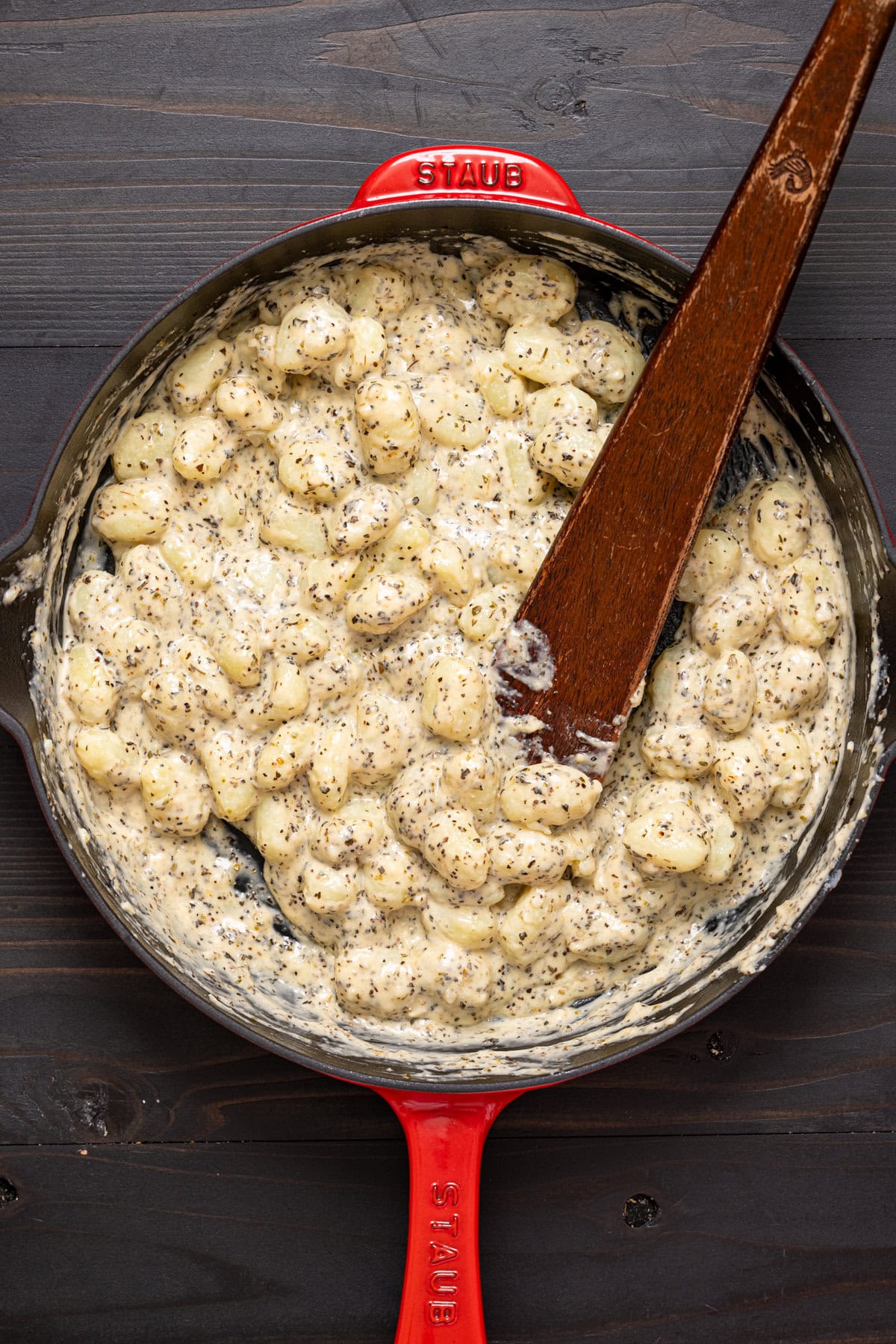 Creamy gnocchi in a red skillet with a wooden spoon.