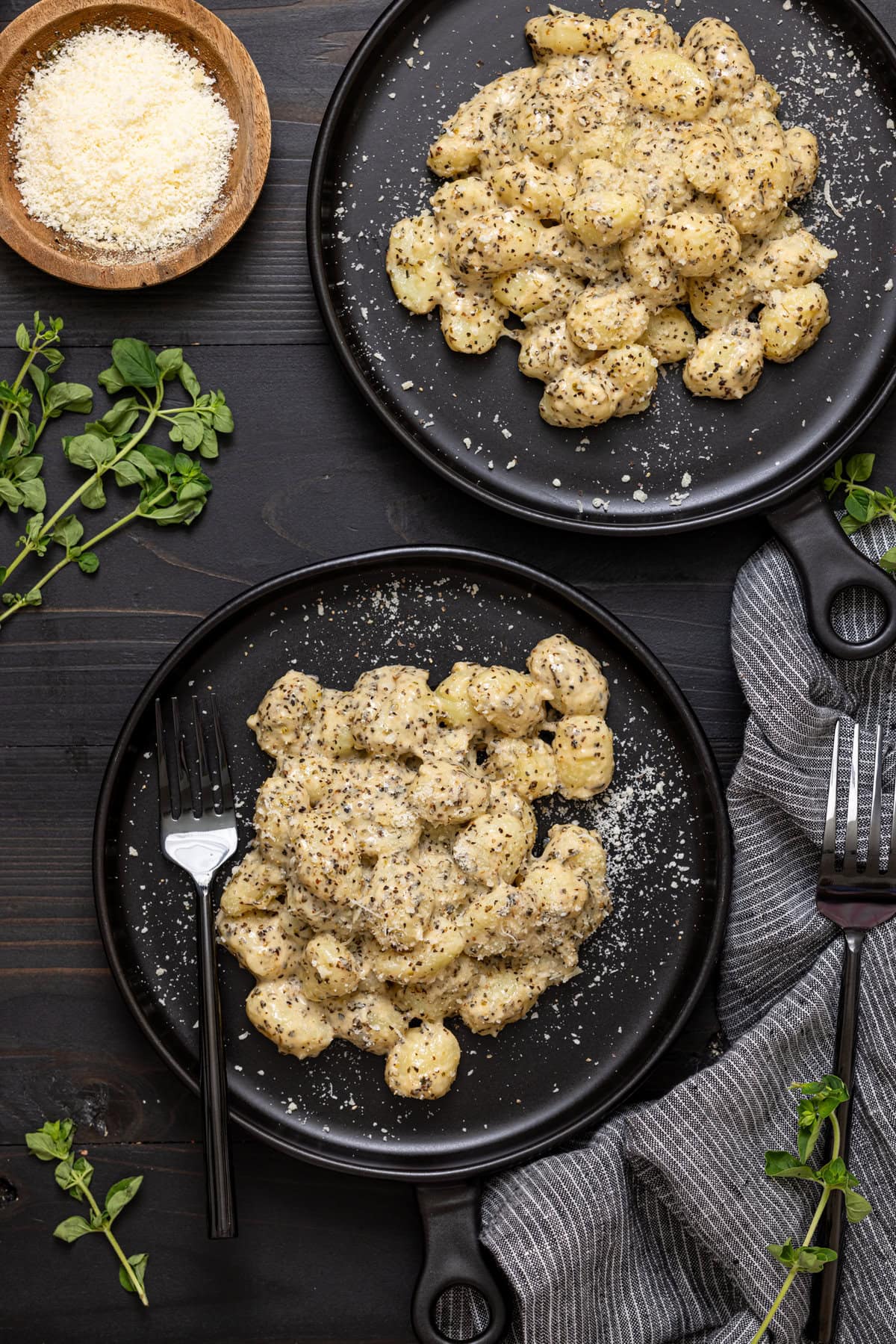 Gnocchi on two plates with parmesan cheese and two forks. 