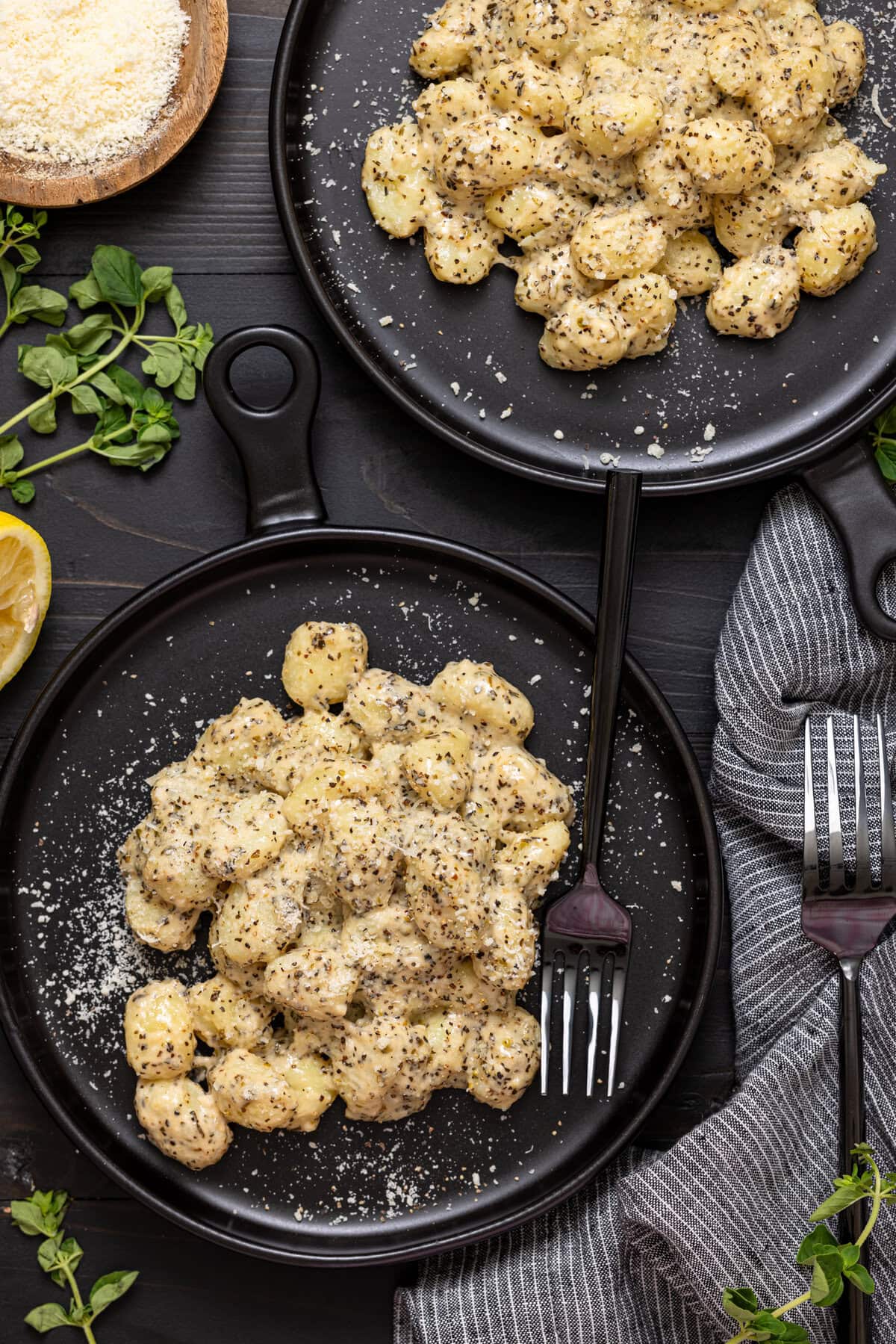 Gnocchi on two black plates with two forks on a black wood table.