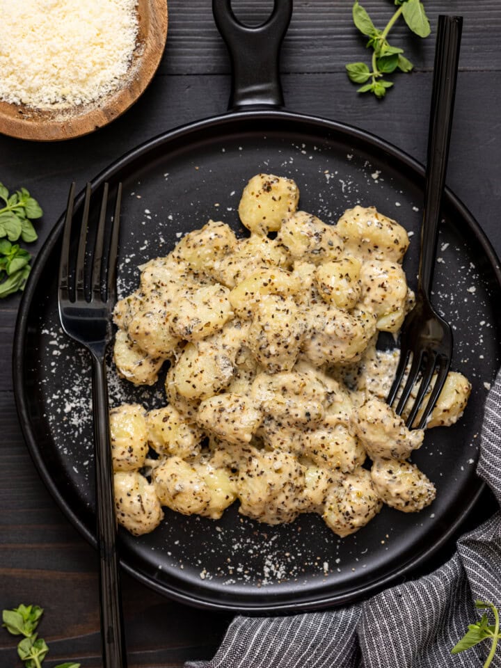 Up close shot of gnocchi on a black plate with two forks and grated parmesan.