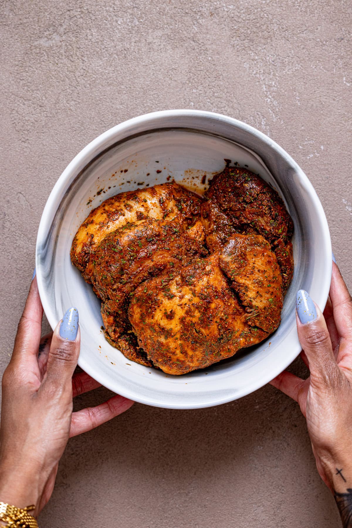 Seasoned chicken in a marble bowl being held with hands.