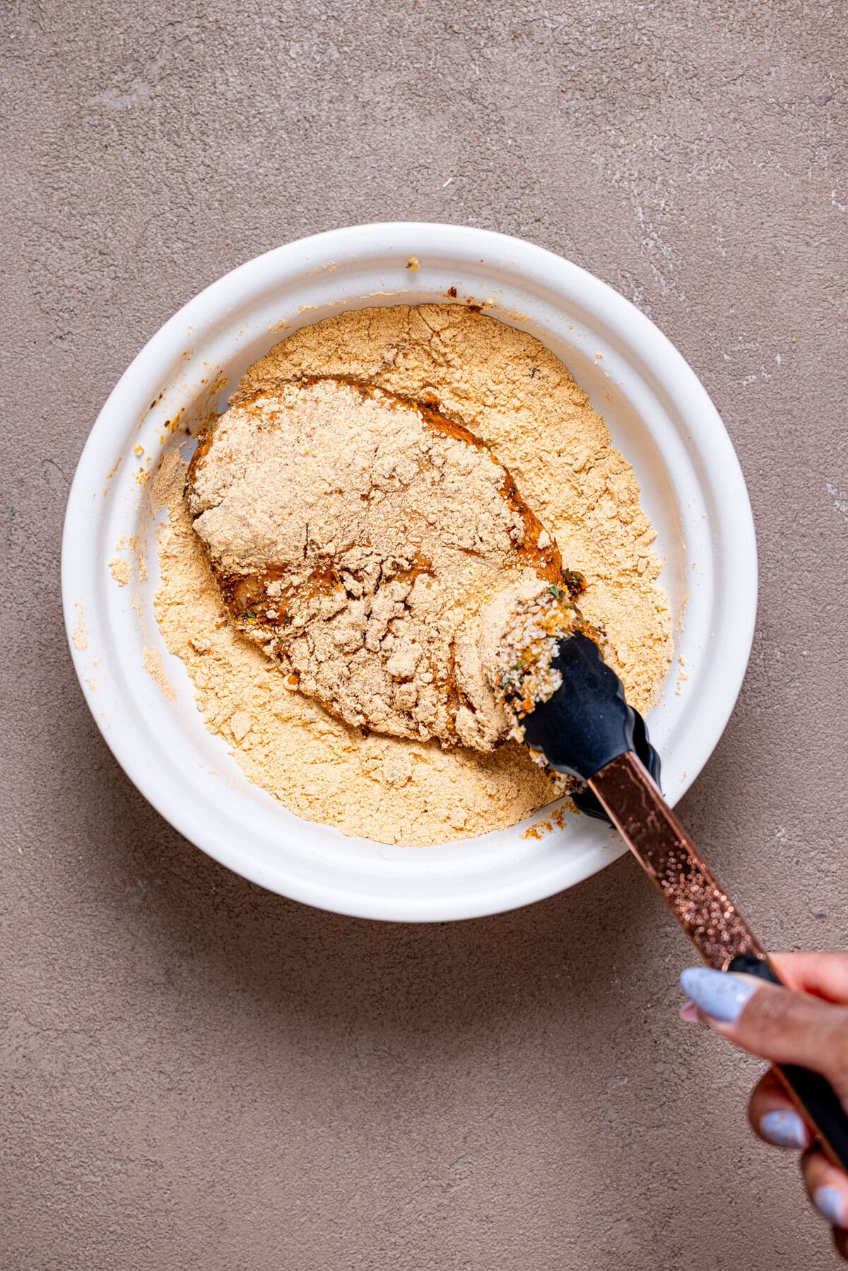 Chicken being dipped in seasoned flour mixture in a bowl.