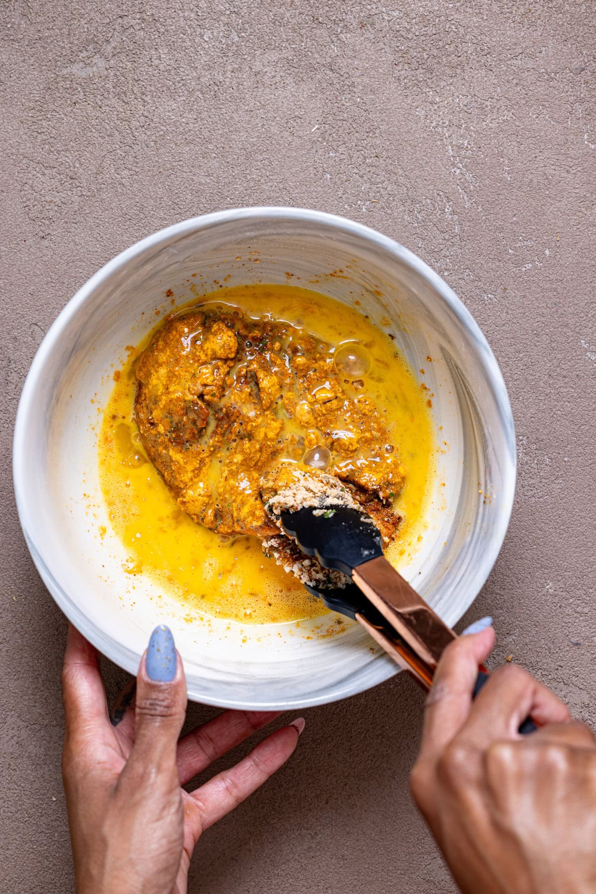 Chicken being dipped in egg mixture in a bowl.