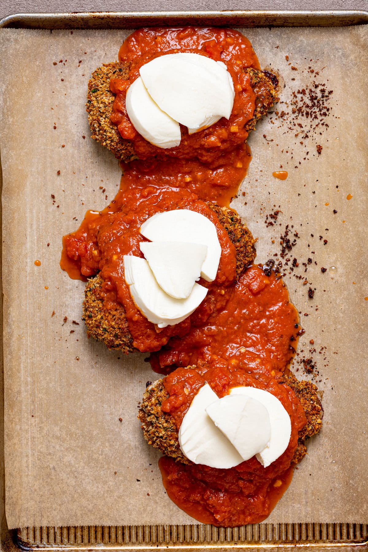 Crispy chicken breasts topped with vodka sauce and sliced mozzarella on a baking sheet with parchment paper.