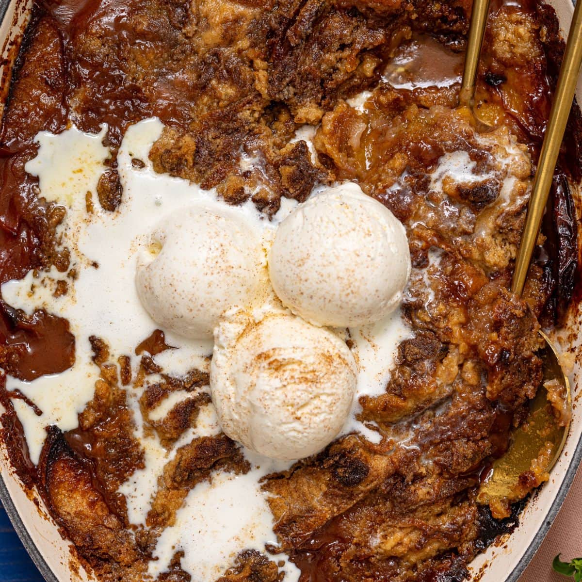 Peach dump cake in a baking dish with serving spoons and ice cream.