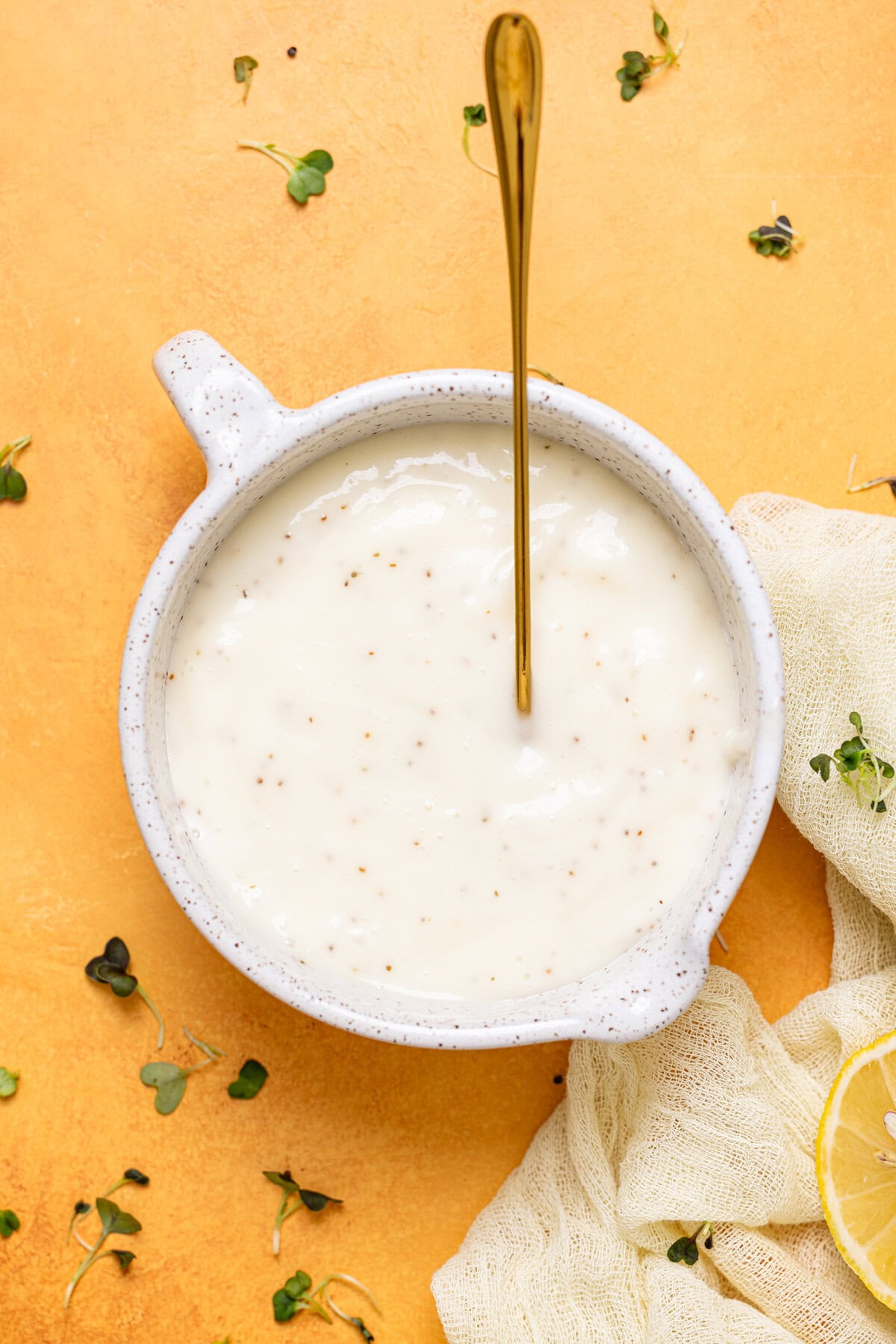 Coleslaw dressing in a bowl with a spoon on a yellow table.