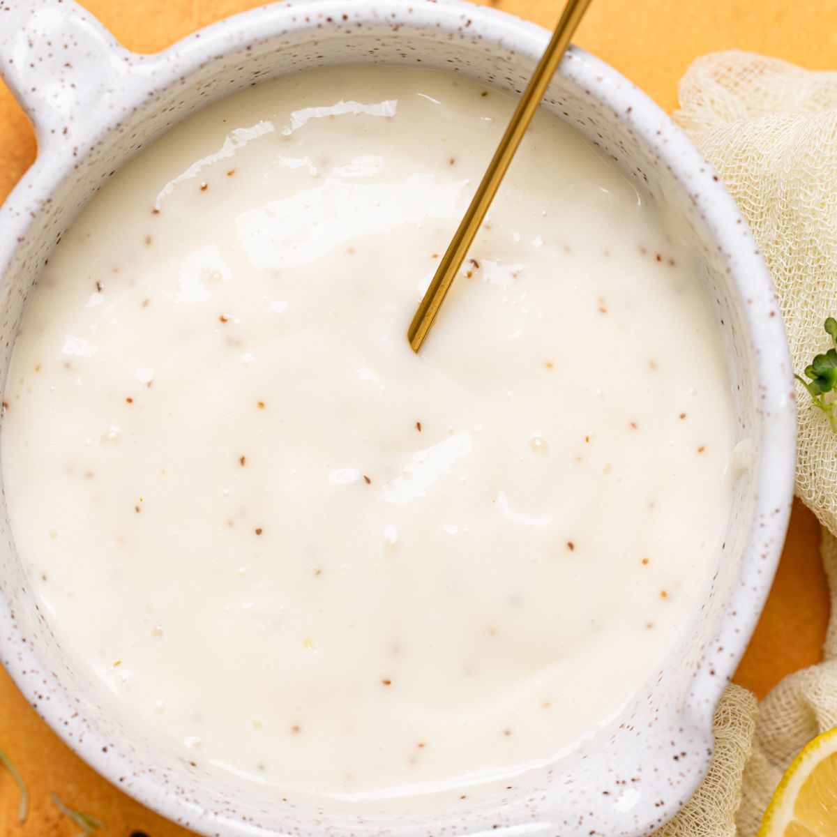 Coleslaw dressing in a white bowl with a spoon on a yellow table.