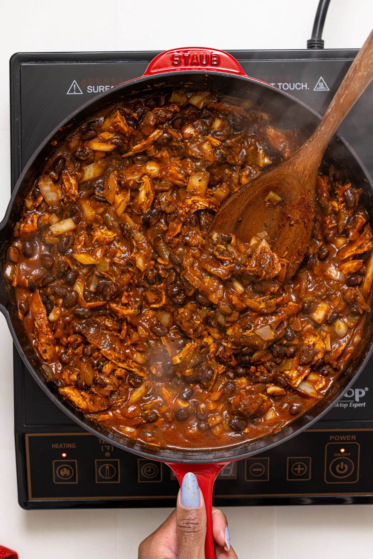 Chicken in enchilada sauce with a wooden spoon on a stovetop.