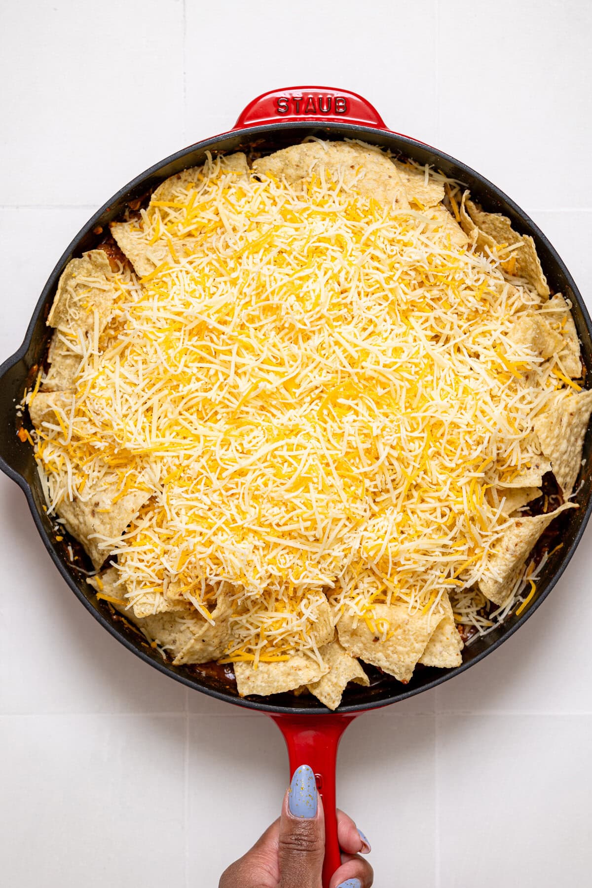 Cheese topped on a enchilada in red skillet being held.