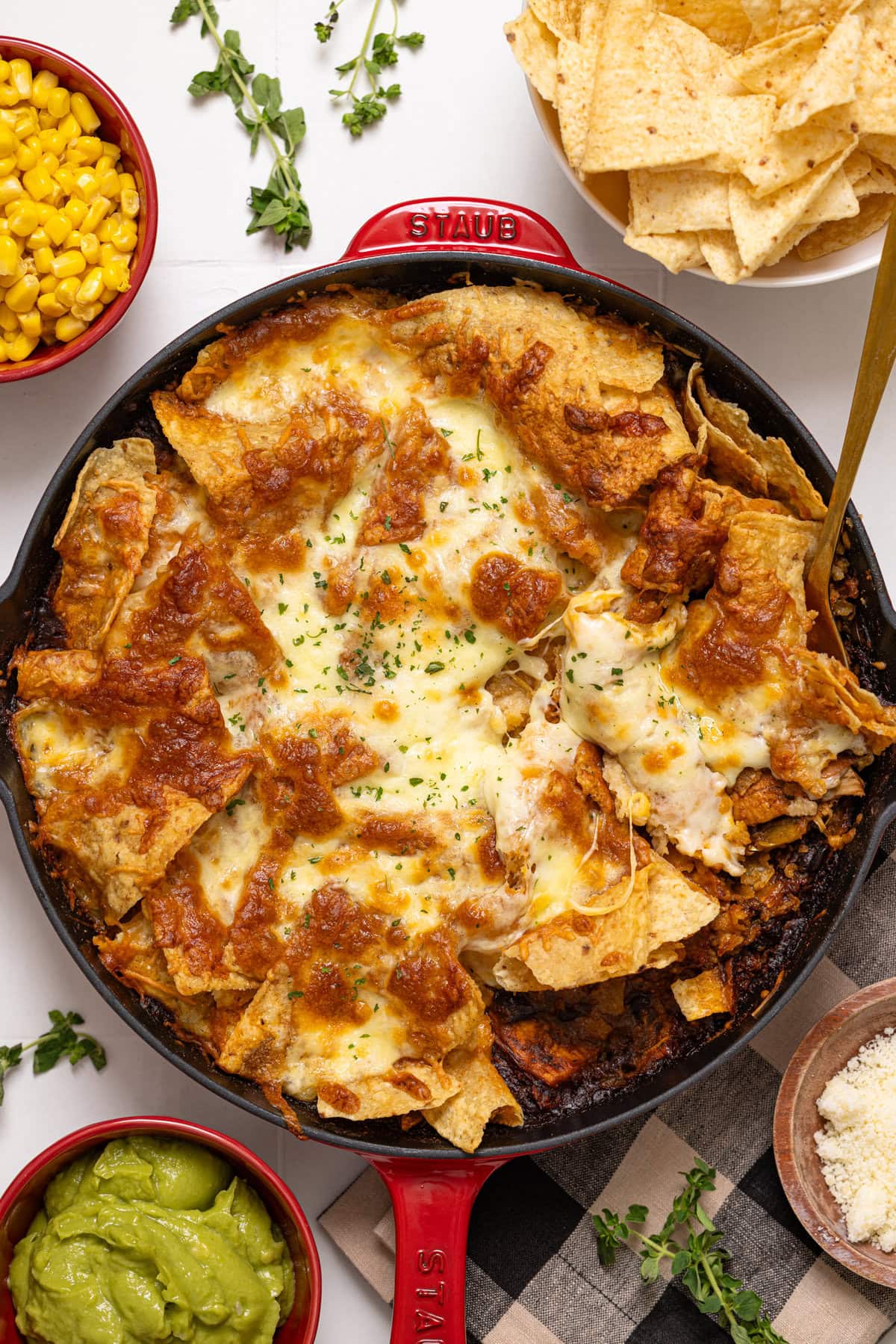 Baked enchilada in a red skillet with a spoon and side of toppings in red bowls.