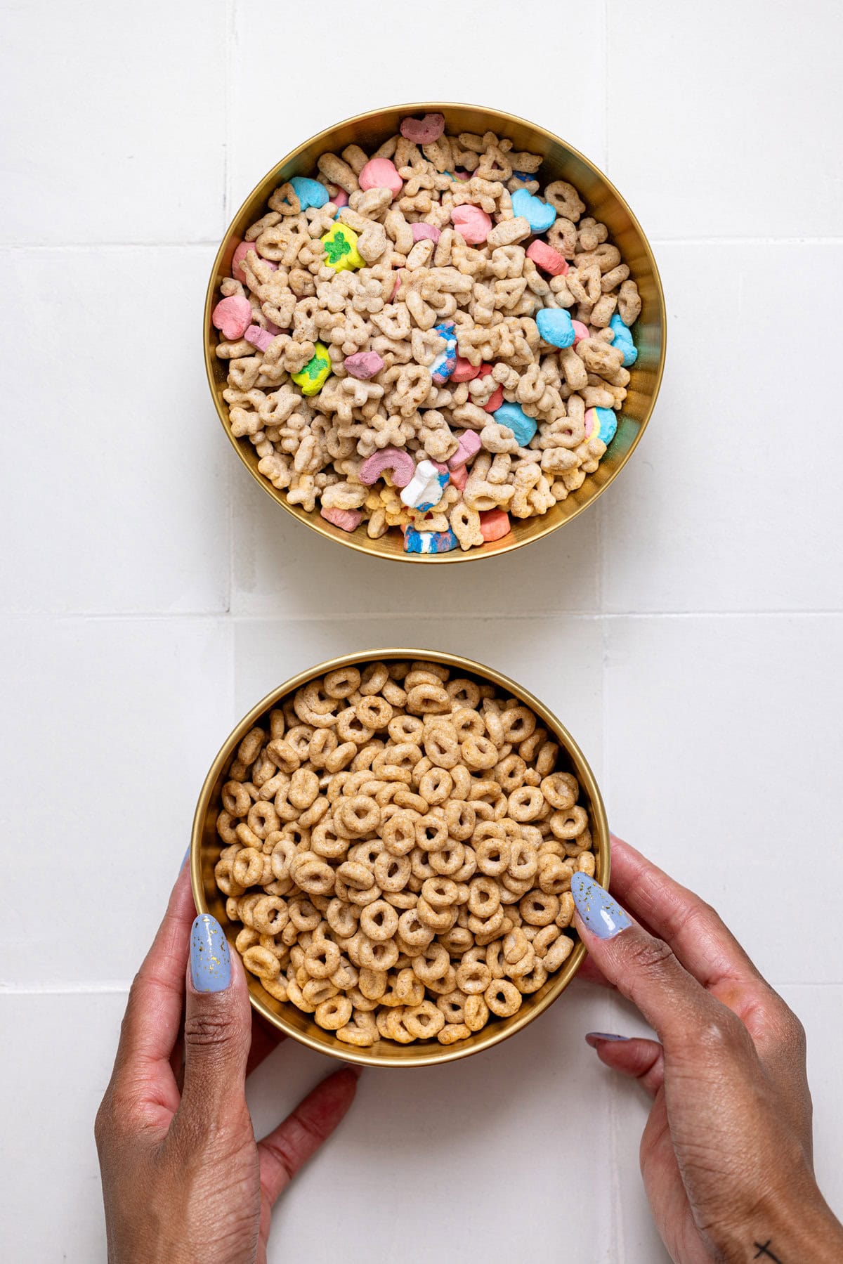 Two bowls of cereal being held on a white tile table with woman hands.