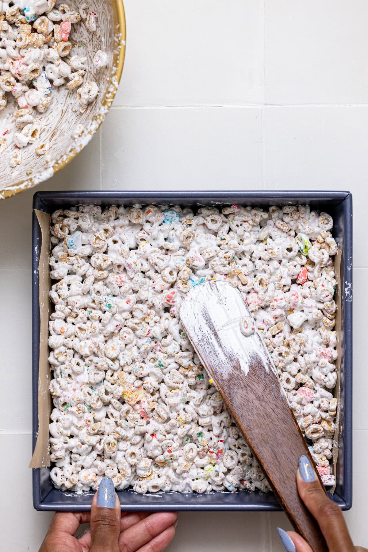 Ingredients being pressed in a square baking pan with a wooden spoon.