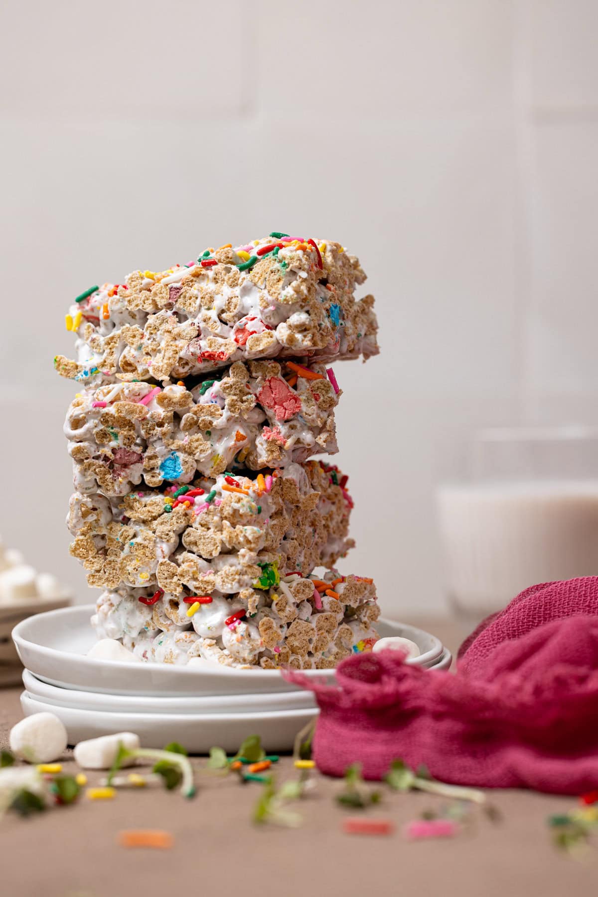 Cereal bars stacked on 3 white plates with a glass of milk.