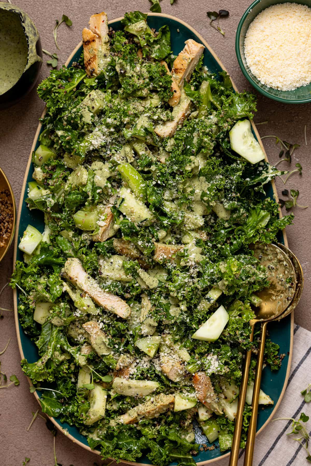 Green goddess chicken salad on a platter with serving spoons and grated parmesan.