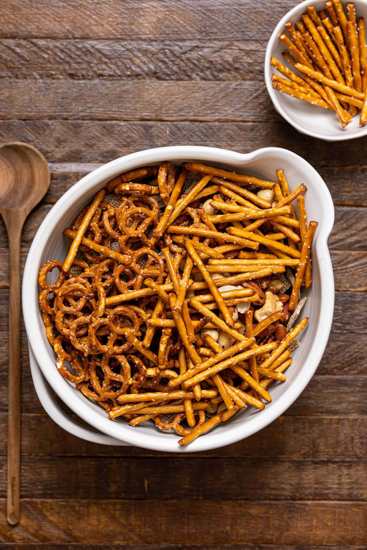 Pretzel mix in a white bowl with a wooden spoon.