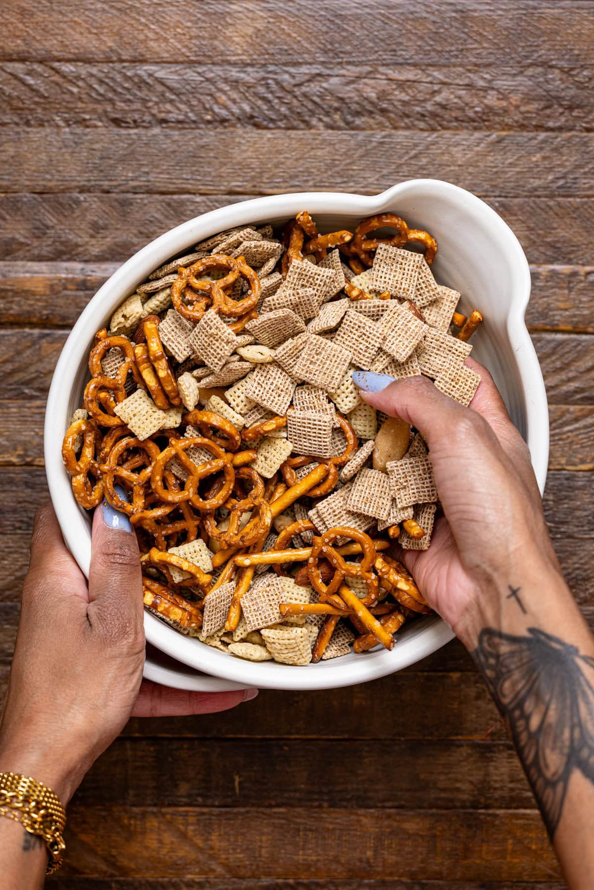 Chex mix being stirred together with hands.