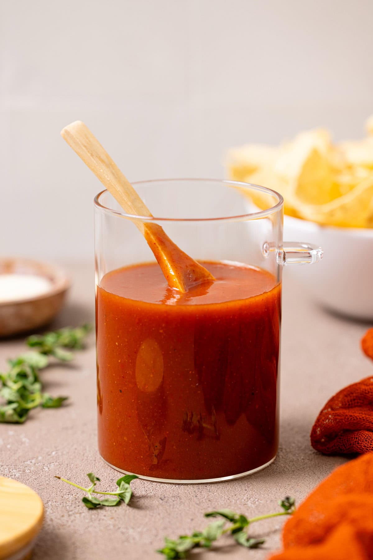 Enchilada sauce in a jar with a spoon and tortilla chips in the background.