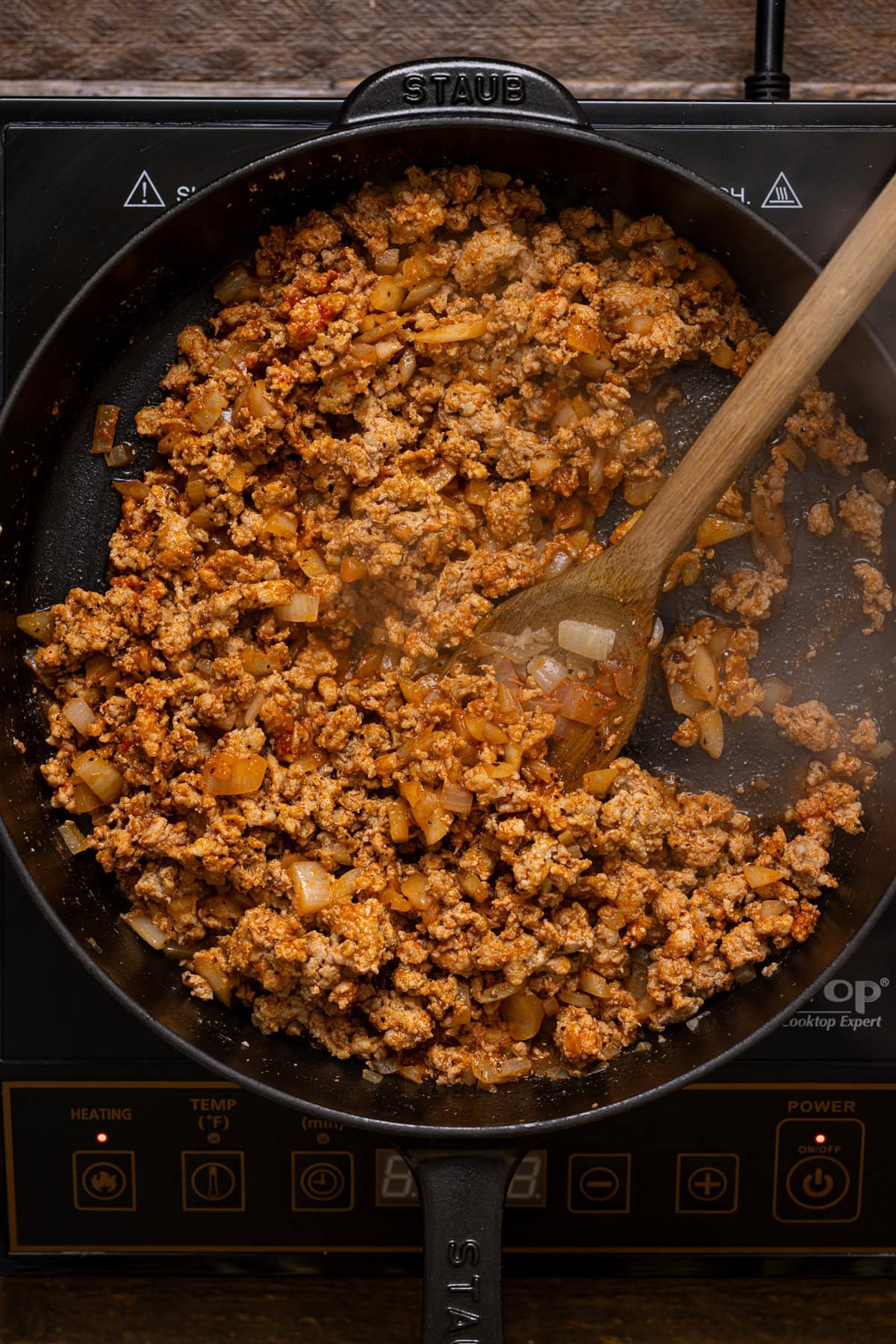 Ground meat being cooked in a black skillet with a wooden spoon.