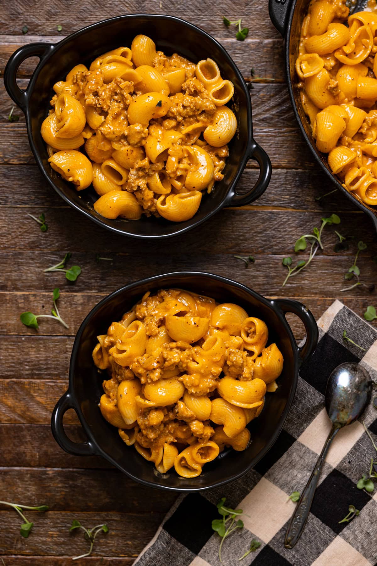 Two black bowls with Hamburger Helper on a brown wood table and a spoon.