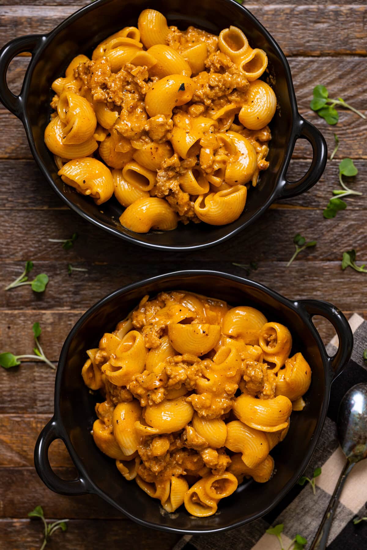 Two bowls of hamburger helper with a spoon on a brown wood table.