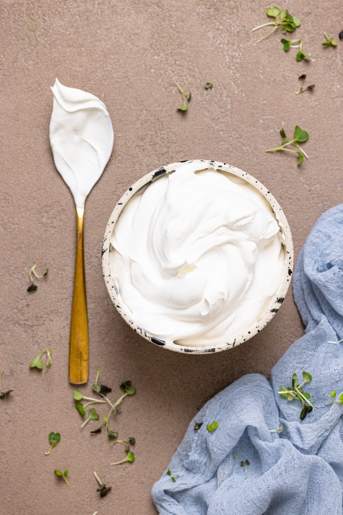 Whipped cream in a bowl on a brown greyish table with a spoon.