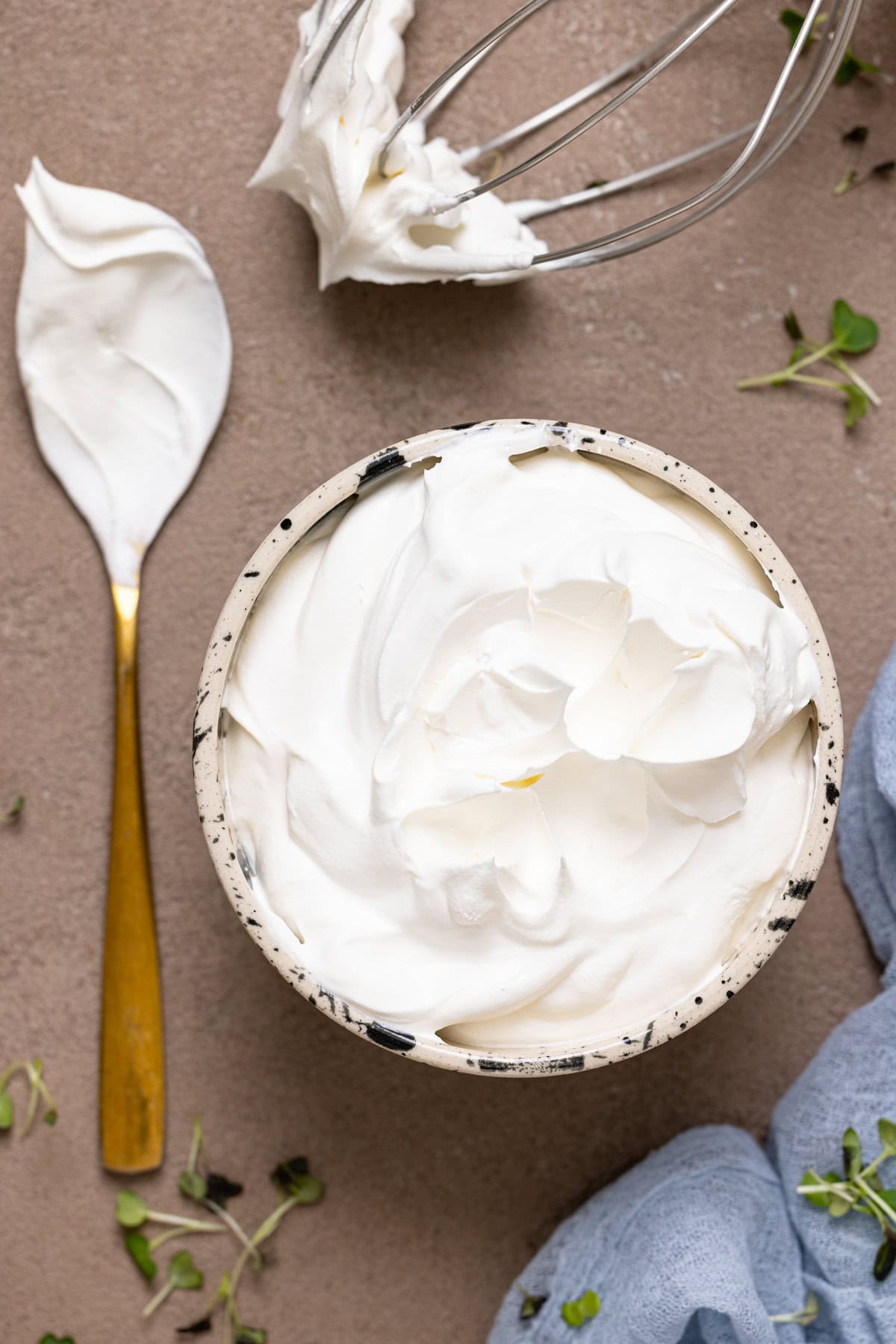 Whipped cream in a bowl with a spoon and mixer whisk.