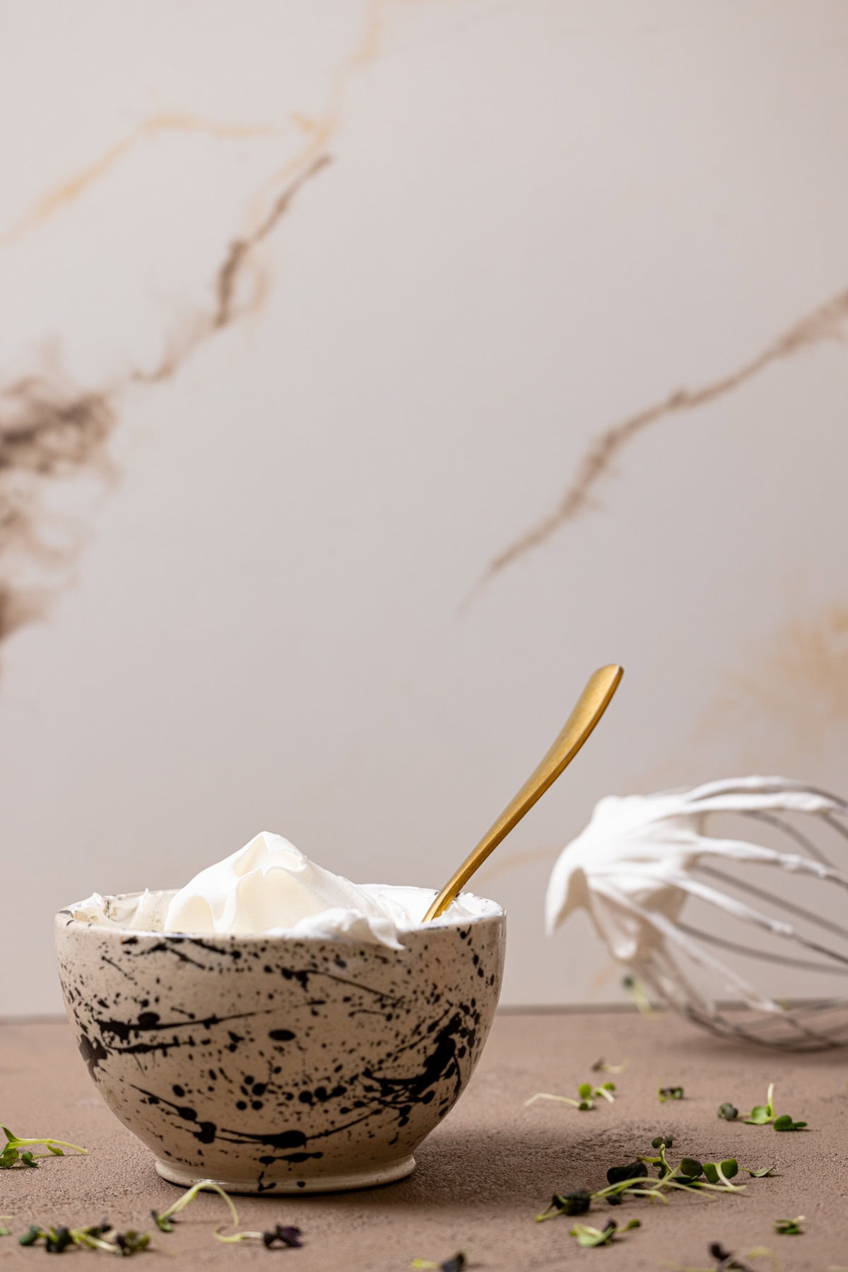 Whipped cream in a black + white bowl and a spoon with a mixer whisk. 