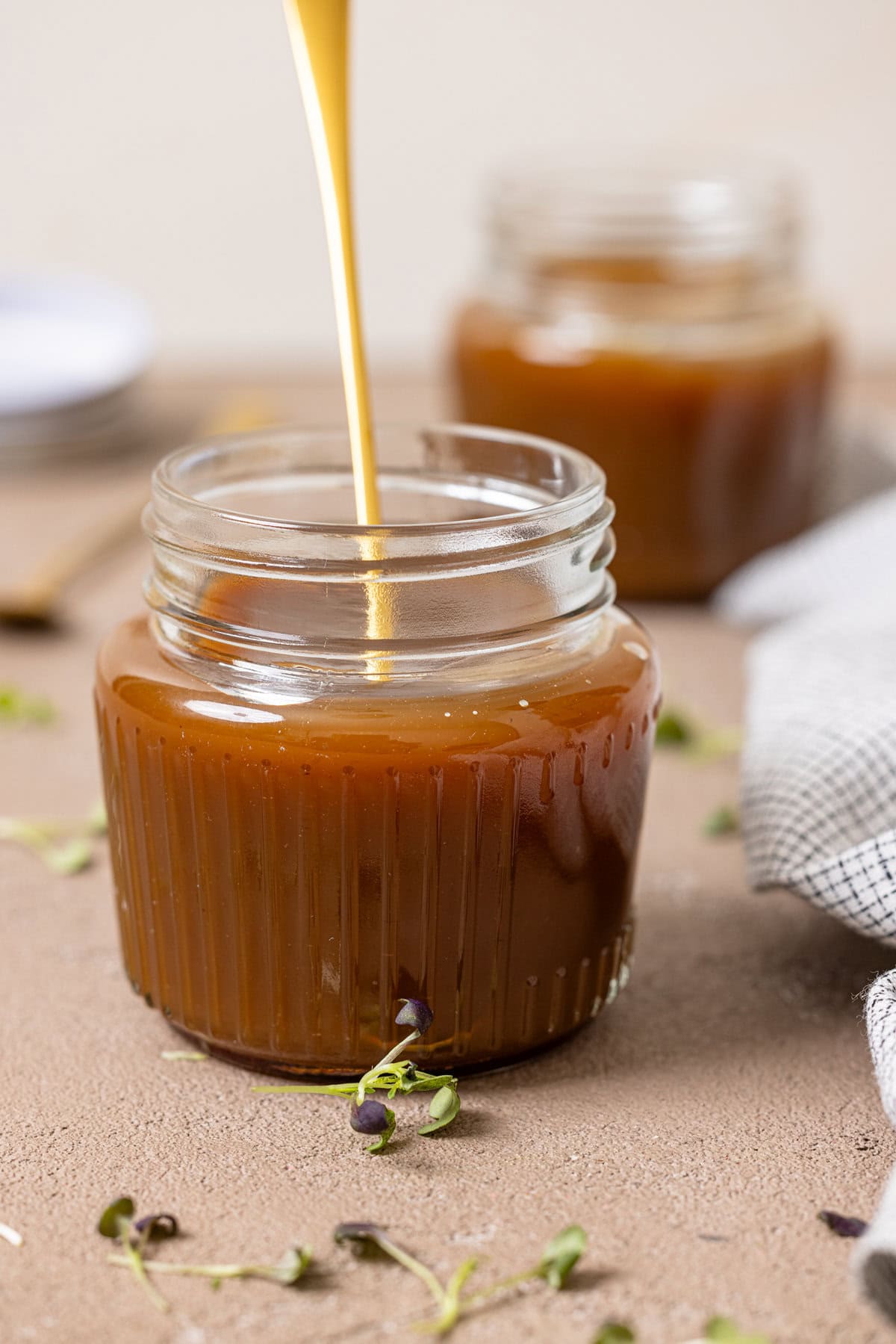 Two mason jars with caramel sauce with a gold spoon.