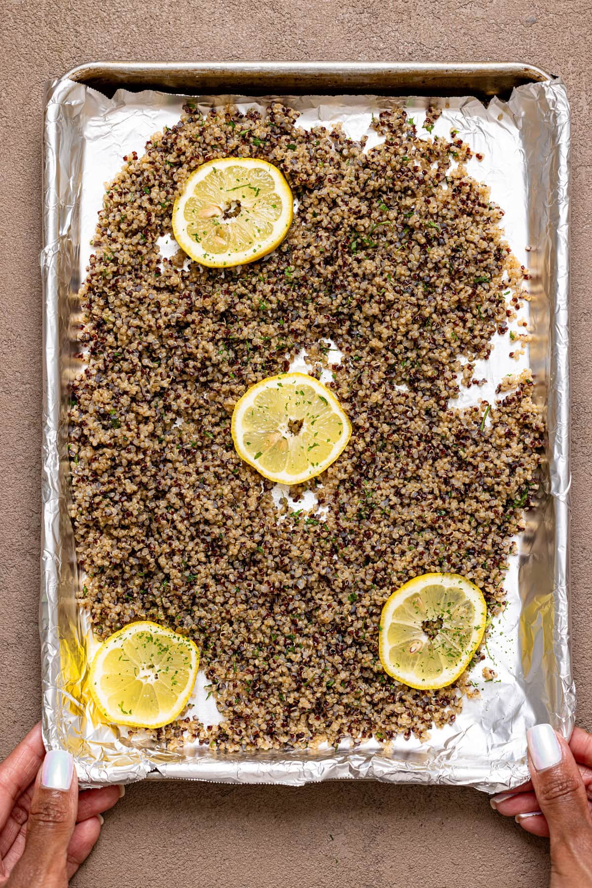 Quinoa spread on a baking sheet with sliced lemons being held.