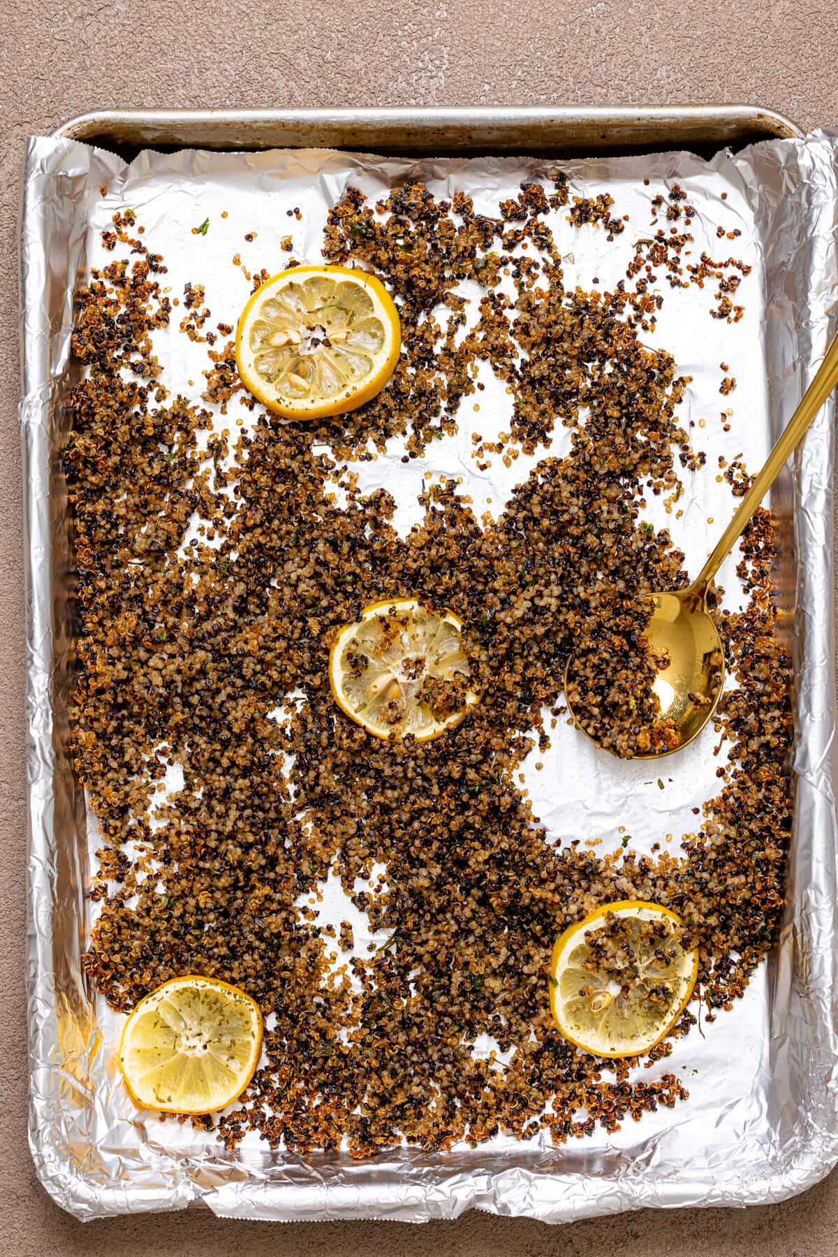 Crispy quinoa baked on a baking sheet with foil paper and lemon slices.