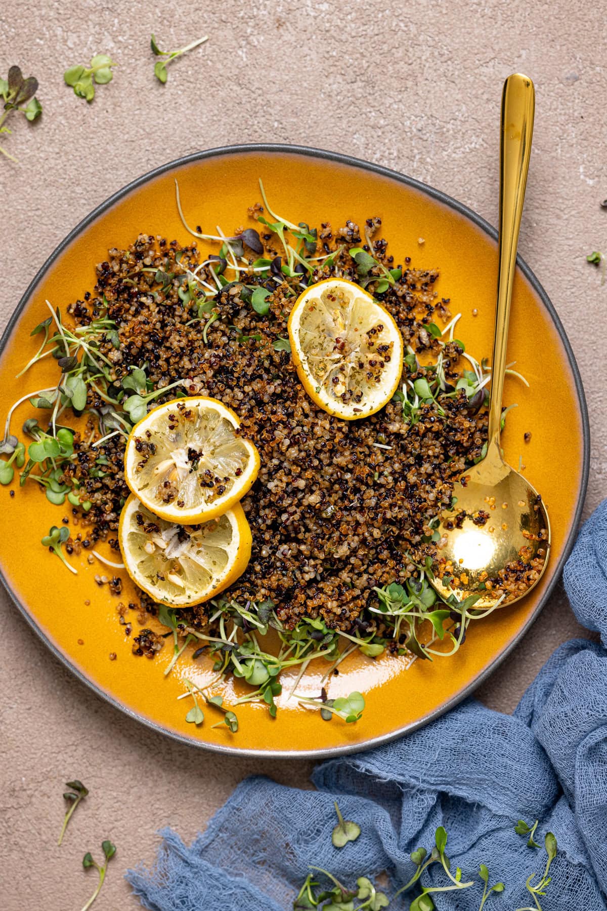 Crispy quinoa on a yellow plate with a spoon, lemon slices, and greens.