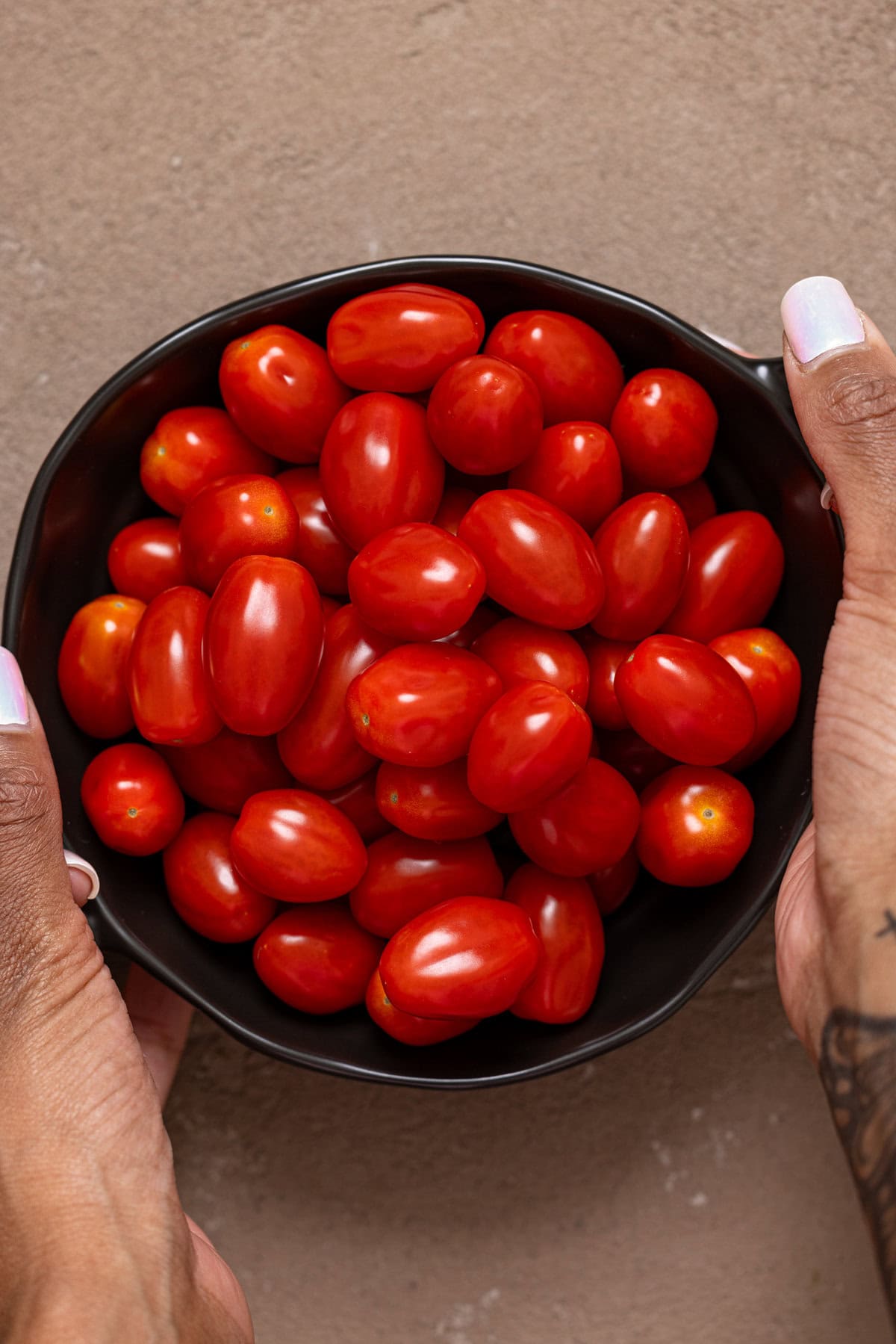 Tomatoes in a black bowl being held.