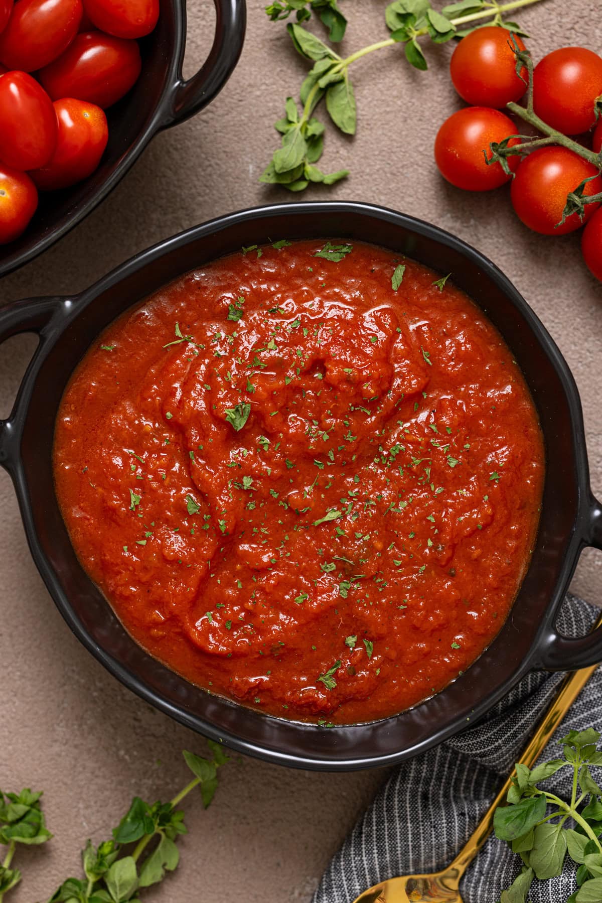 Up close shot of tomato sauce in a black bowl with tomatoes. 